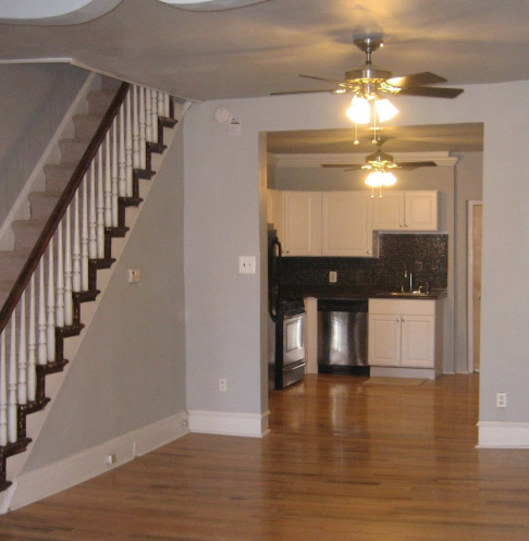 Renovated living room with fresh paint, hardwood floors, a ceiling fan, and a view into a modern kitchen.